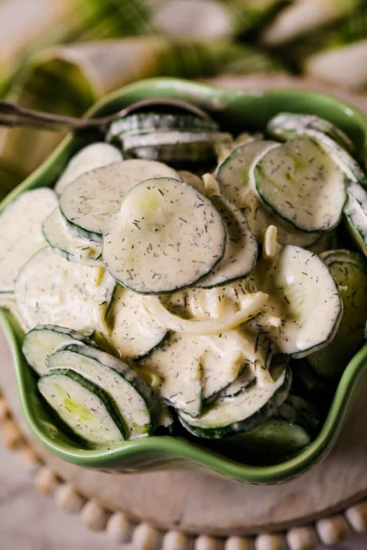 A green bowl filled with Cucumber Onion Salad—sliced cucumbers and onions coated in a creamy dill dressing.