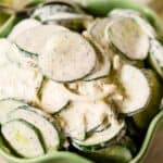 A green bowl filled with Cucumber Onion Salad, featuring sliced cucumbers and onions coated in a creamy dill dressing.