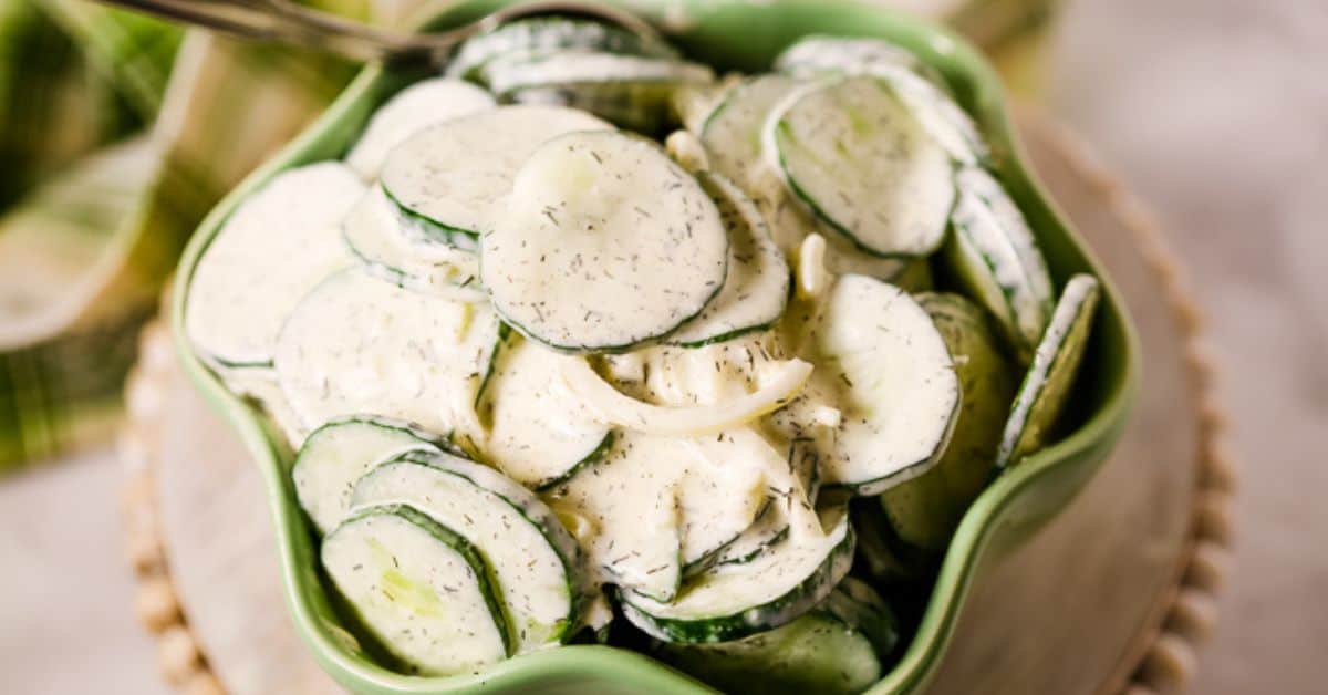 A green bowl filled with Cucumber Onion Salad, featuring sliced cucumbers and onions coated in a creamy dill dressing.