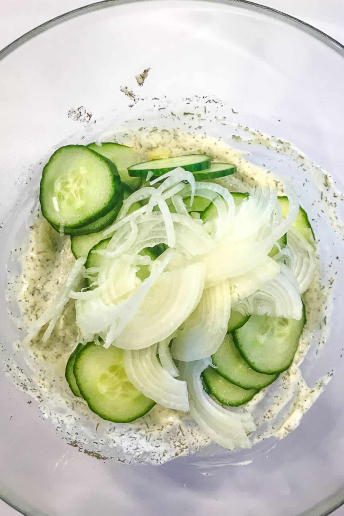 Cucumber Onion Salad features sliced cucumbers and onions in a glass bowl, tossed with a creamy dressing and fresh herbs.