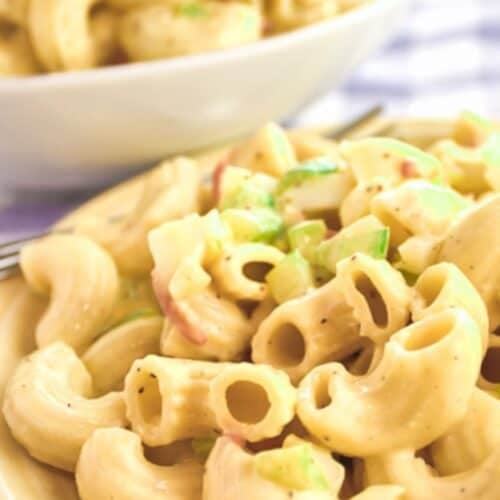 Close-up of creamy Easy Macaroni Salad Recipe with chopped green onions and vegetables on a plate, with another bowl of macaroni salad in the background.