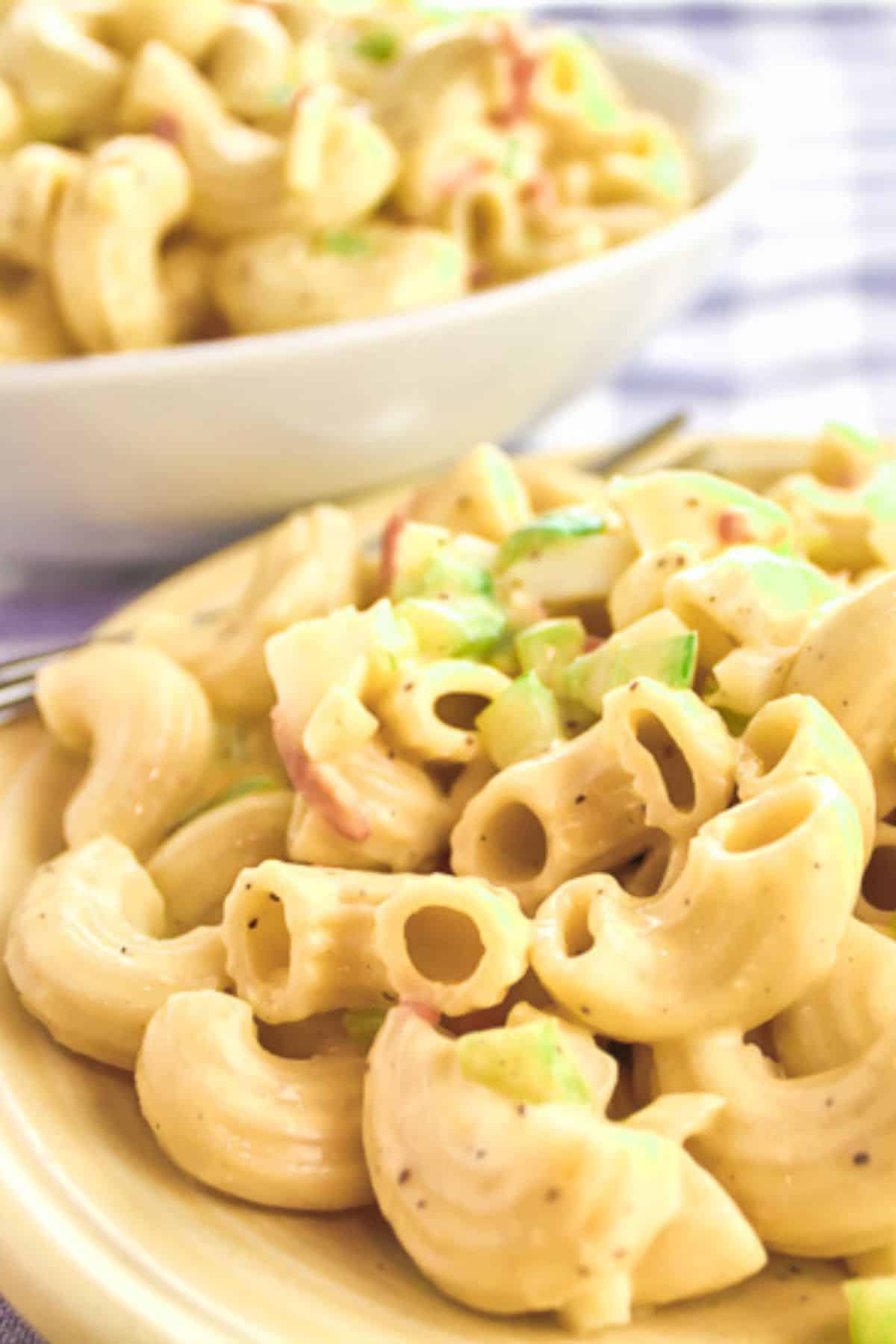 Close-up of creamy Easy Macaroni Salad Recipe with chopped green onions and vegetables on a plate, with another bowl of macaroni salad in the background.