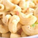 Close-up of Recipe featuring elbow pasta, diced celery, and creamy dressing, garnished with pepper and small bits of vegetables.