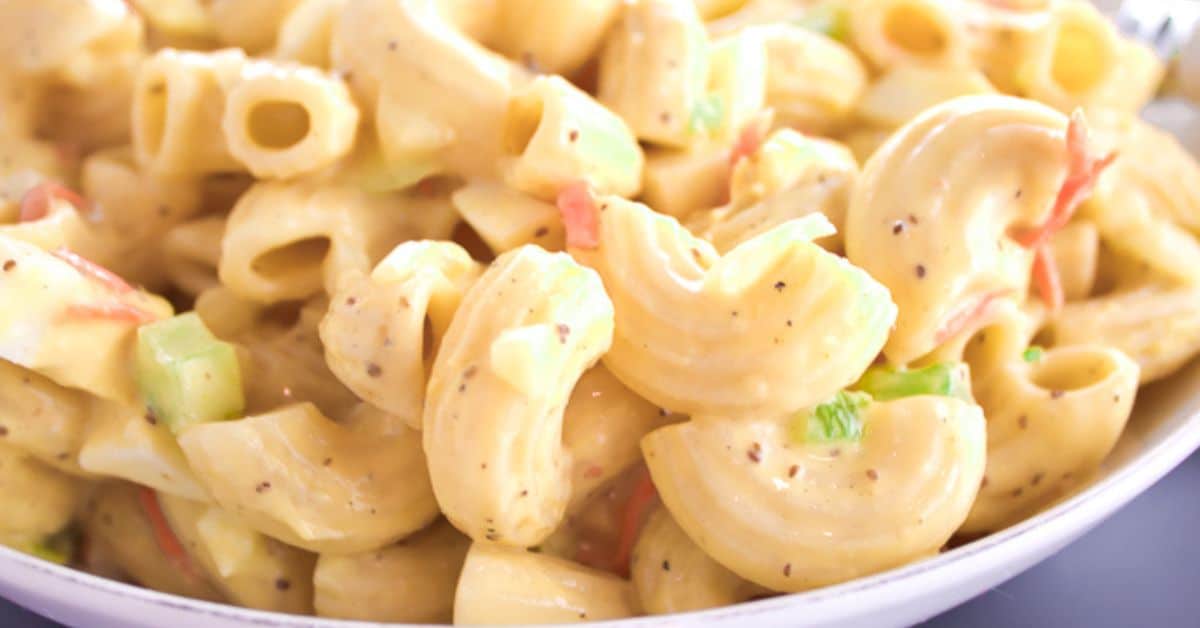 Close-up of Recipe featuring elbow pasta, diced celery, and creamy dressing, garnished with pepper and small bits of vegetables.