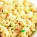 A close-up of this Easy Macaroni Salad Recipe shows elbow pasta, chopped celery, and peppers in a creamy dressing, served in a white bowl.