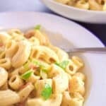 Close-up of an Easy Macaroni Salad Recipe, showcasing creamy macaroni mixed with chopped green bell peppers and red pieces, with a bowl of extra salad in the background.