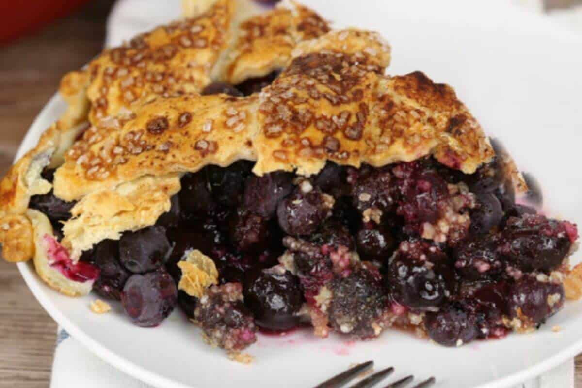 Blueberry Pie with lattice crust on a white plate with fork.
