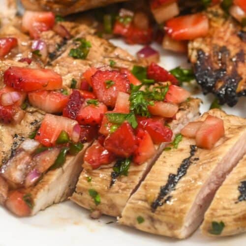 Grilled Balsamic Chicken breast sliced and topped with a fresh strawberry salsa, served on a white plate.