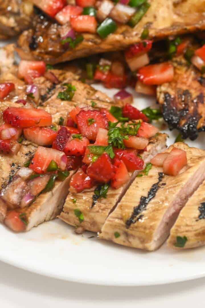 Grilled Balsamic Chicken breast sliced and topped with a fresh strawberry salsa, served on a white plate.