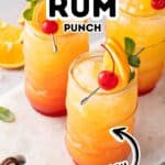 Three glasses of Jamaican rum punch garnished with orange slices, cherries, and mint rest on a marble board, with text overlay reading "Jamaican Rum Punch Easy.