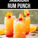Three glasses of Jamaican rum punch garnished with orange slices, cherries, and mint rest on a marble surface with extra orange slices in the background. The text above reads, "Refreshing Jamaican Rum Punch.