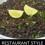 A bowl of Mexican black beans garnished with lime wedges and chopped cilantro, labeled "restaurant-style Mexican black beans.