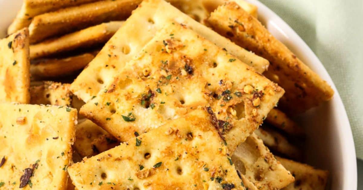 A bowl filled with seasoned saltine crackers, topped with visible herbs and spices—a perfect Spicy Crackers Recipe for snack lovers.