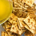 A pile of squares on a plate next to a glass bowl containing dip.