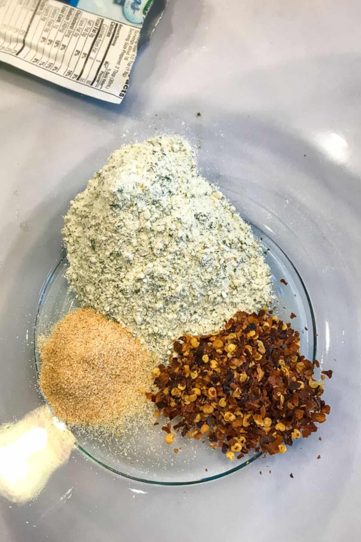Three piles of dry ingredients—powdered seasoning, granulated garlic, and crushed red pepper flakes—on a clear glass plate, ready to add bold flavor to your Spicy Crackers Recipe.