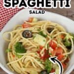 A bowl of Spaghetti Pasta Salad with spaghetti, tomatoes, olives, broccoli, and parsley sits on a table beside a red-checkered napkin. Text reads "California Spaghetti Salad Easy.