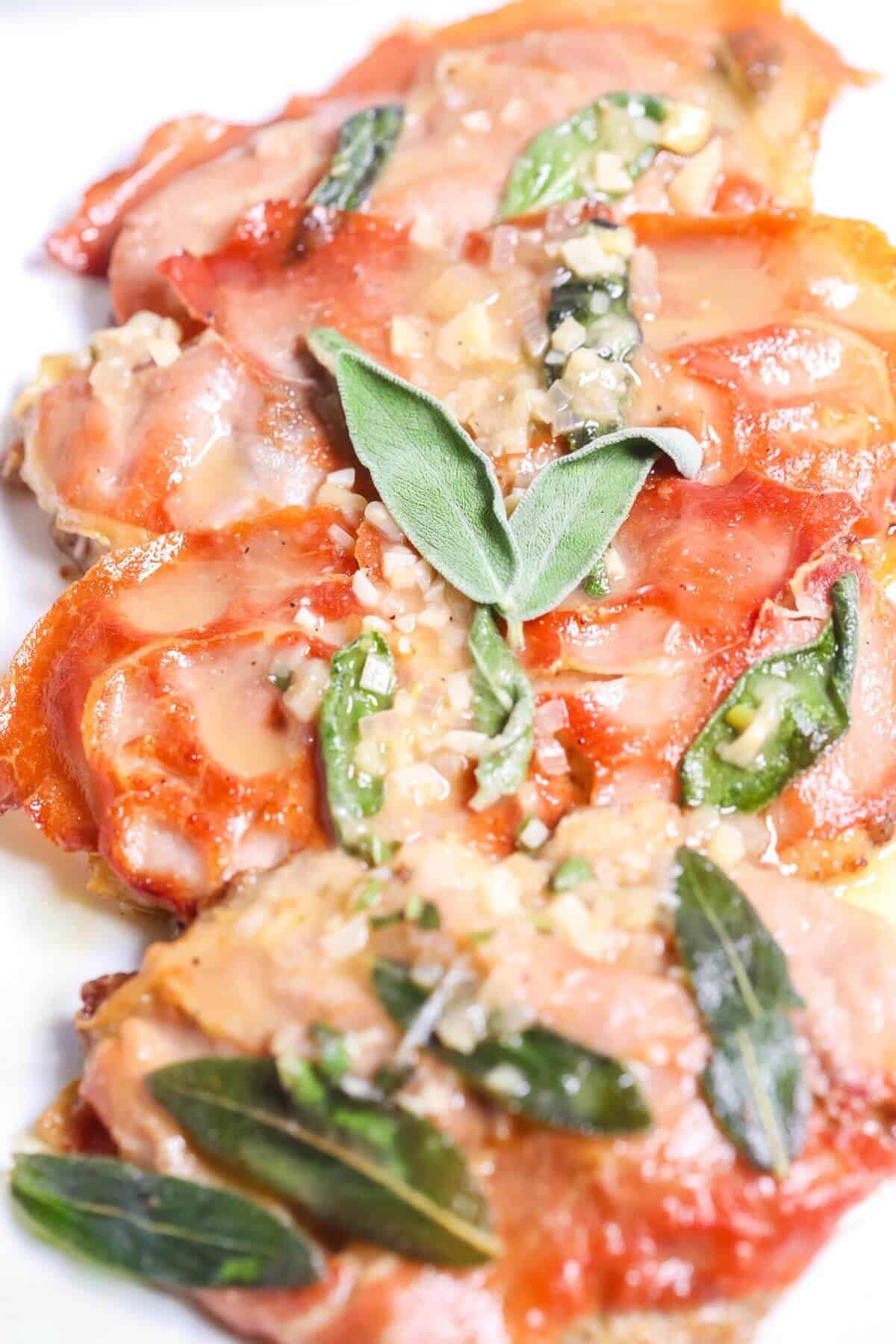 A plate of saltimbocca, featuring slices of chicken topped with prosciutto, fresh sage leaves, and a light sauce, reminiscent of the classic veal saltimbocca.