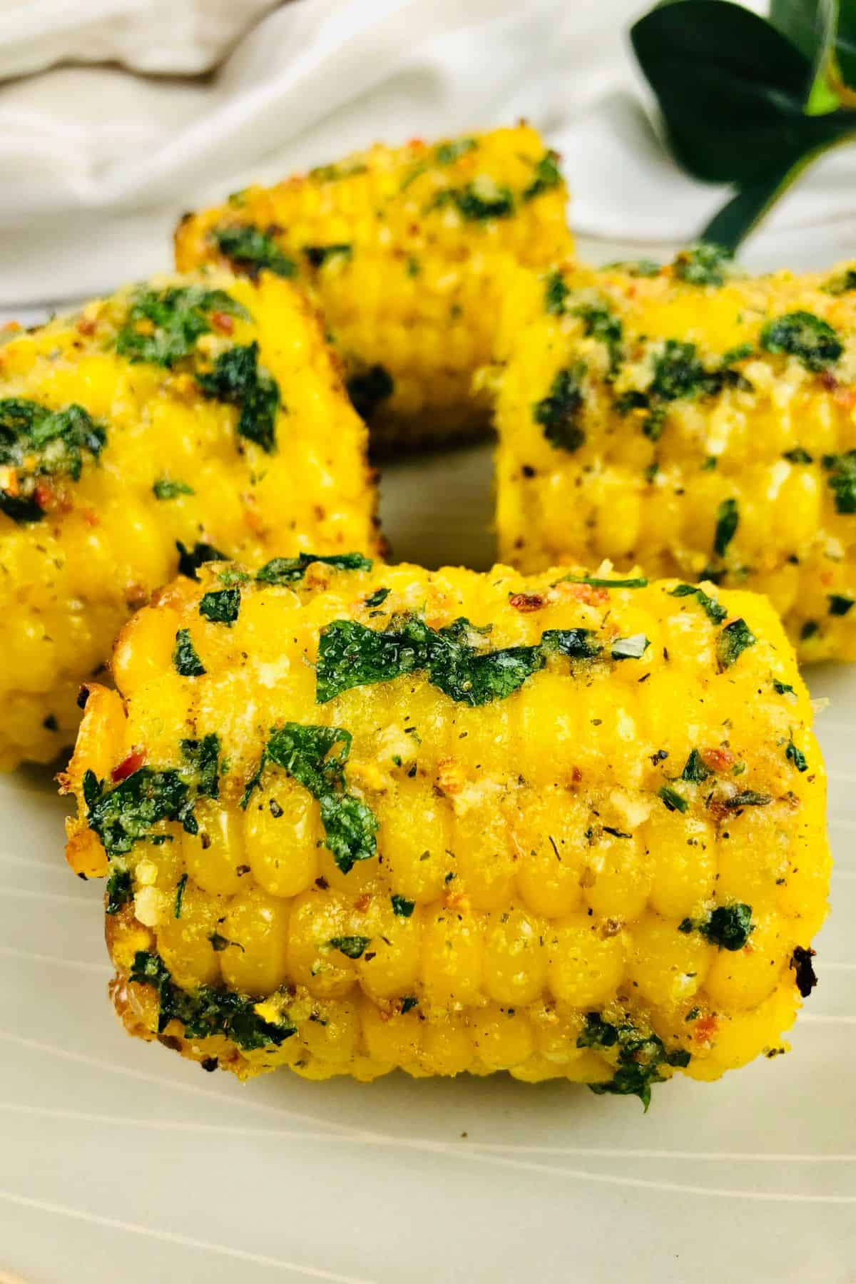 Four pieces of Air Fryer Corn on the Cob coated with herbs and spices are arranged on a plate.