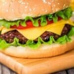 A cheeseburger with lettuce, tomato, and cheddar cheese in a sesame seed bun sits on a wooden board, showcasing a classic take on baked hamburgers.