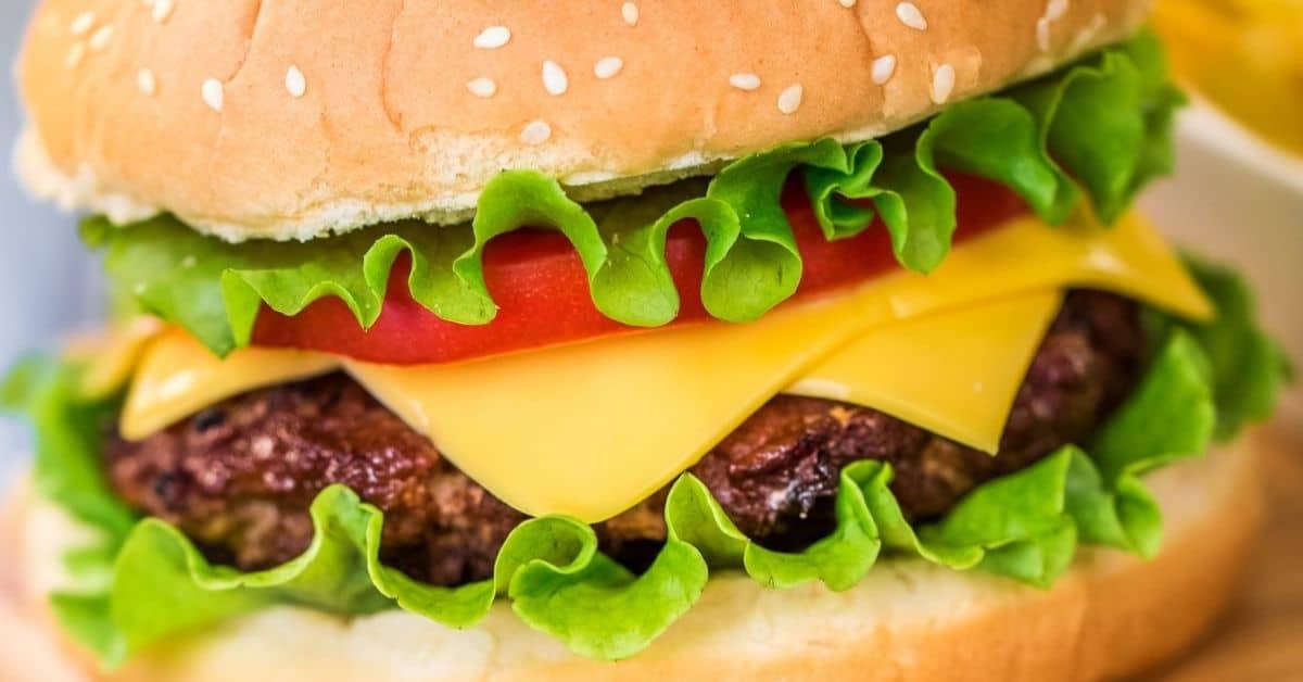 Close-up of a delicious Baked Hamburger with lettuce, tomato, cheddar cheese, and a beef patty in a sesame seed bun.