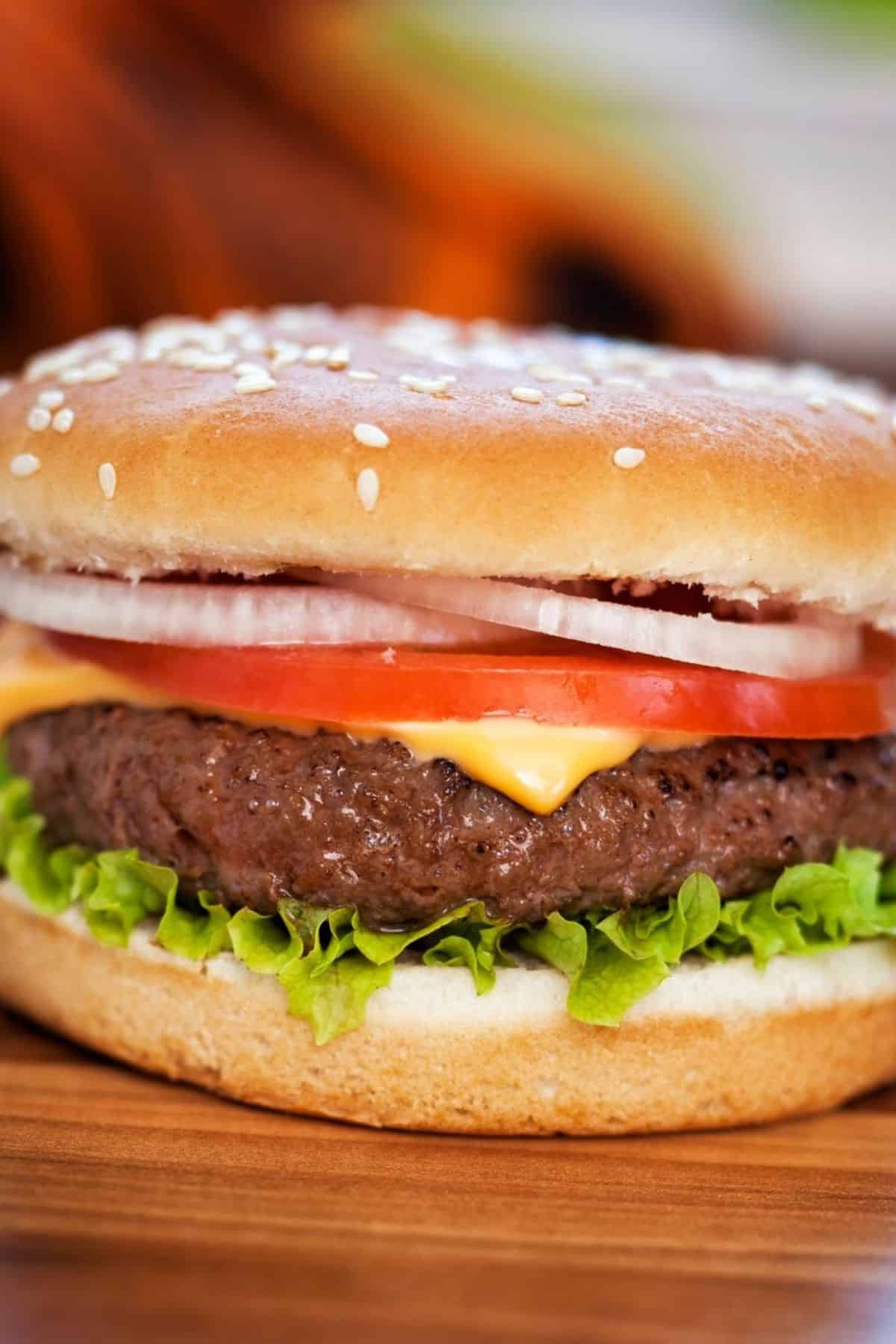 A finished burger in the oven with cheese lettuce, tomato and onion.