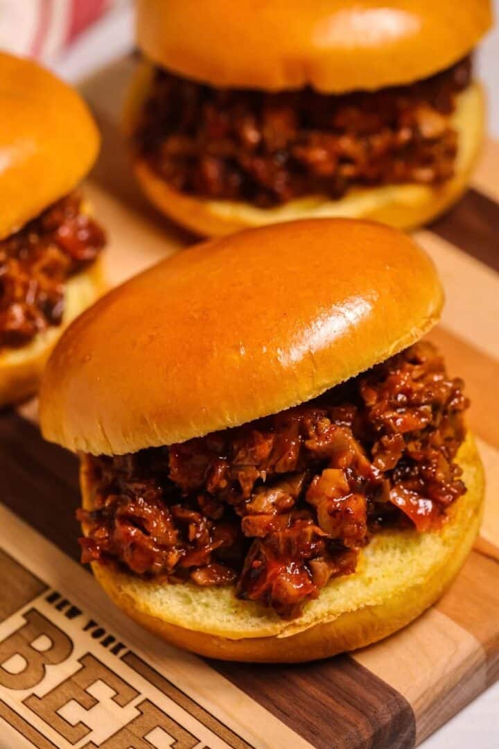 Two beef brisket sloppy joe sandwiches on brioche buns served on a wooden cutting board.