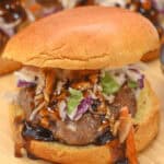 A close-up of a pork burger with a brioche bun, topped with mixed greens and drizzled with a dark sauce.