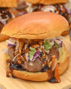 A close-up of a pork burger with a brioche bun, topped with mixed greens and drizzled with a dark sauce.