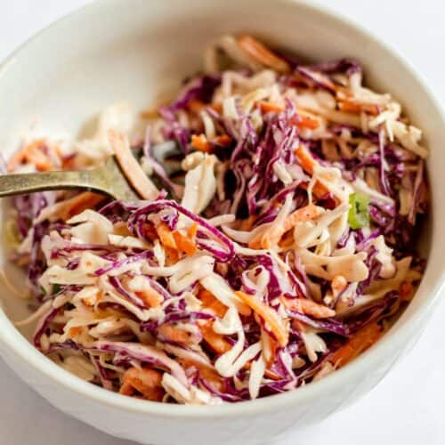A white bowl filled with Southern Coleslaw made of shredded red and green cabbage and carrots, mixed with a creamy dressing, with a fork inside.