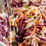 Close-up of a bowl of Southern Coleslaw with shredded red and green cabbage, carrots, and green onions, with metal tongs in the bowl.