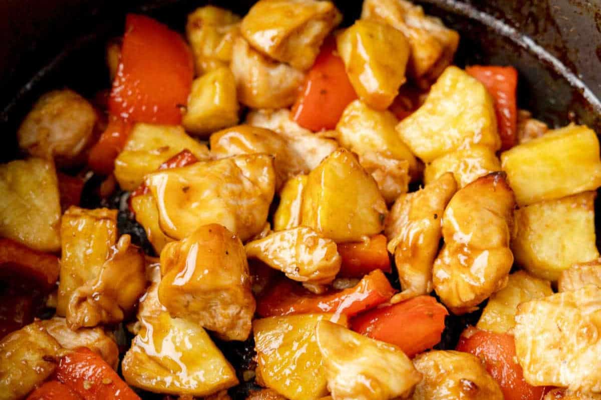 Close-up of sweet and sour chicken, a standout among pineapple dishes, featuring chunks of pineapple, red bell pepper, and chicken coated in a glossy sauce.