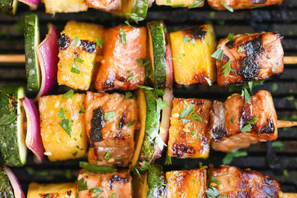 Grilled salmon kabob skewers with zucchini, pineapple, and red onion, garnished with herbs and arranged on a grill—perfect for adding to your favorite kabob recipes.