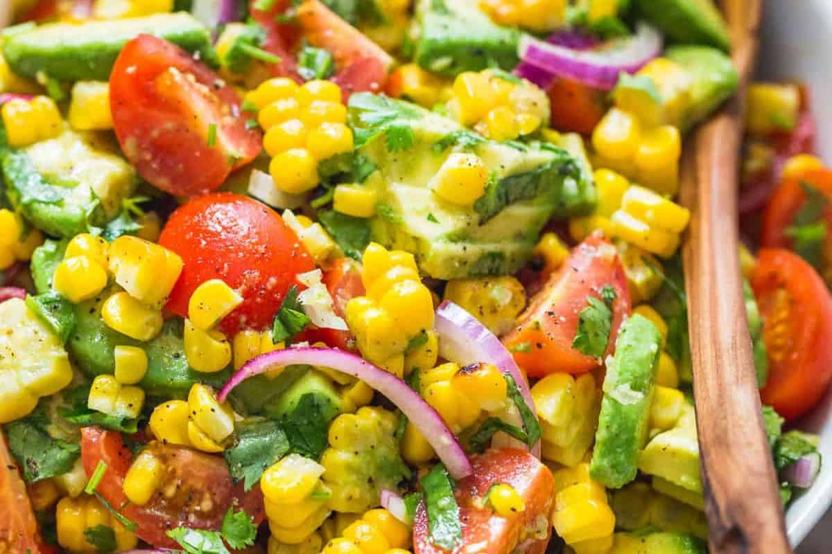 A close-up of a colorful summer salad with corn, avocado, cherry tomatoes, red onion, and cilantro, tossed together and lightly seasoned—a perfect addition to your mouthwatering salads collection.