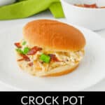 A sandwich with chicken, bacon, and green onions in a bun sits on a white plate. Text reads "Crock Pot Cracked Chicken Sandwiches.