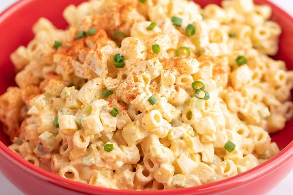 A bowl of creamy macaroni salad, one of the most mouthwatering salads, topped with chopped green onions and a sprinkle of paprika.