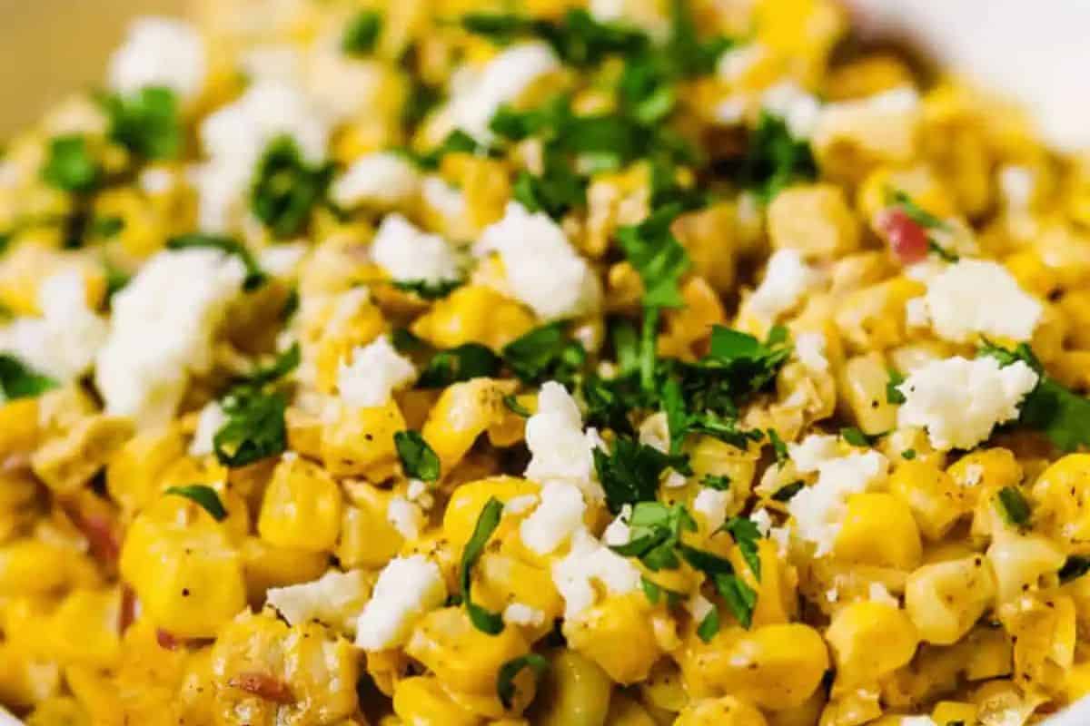 Close-up of a corn dish topped with crumbled cheese and chopped fresh herbs—perfect for summer salads or as a vibrant BBQ side.