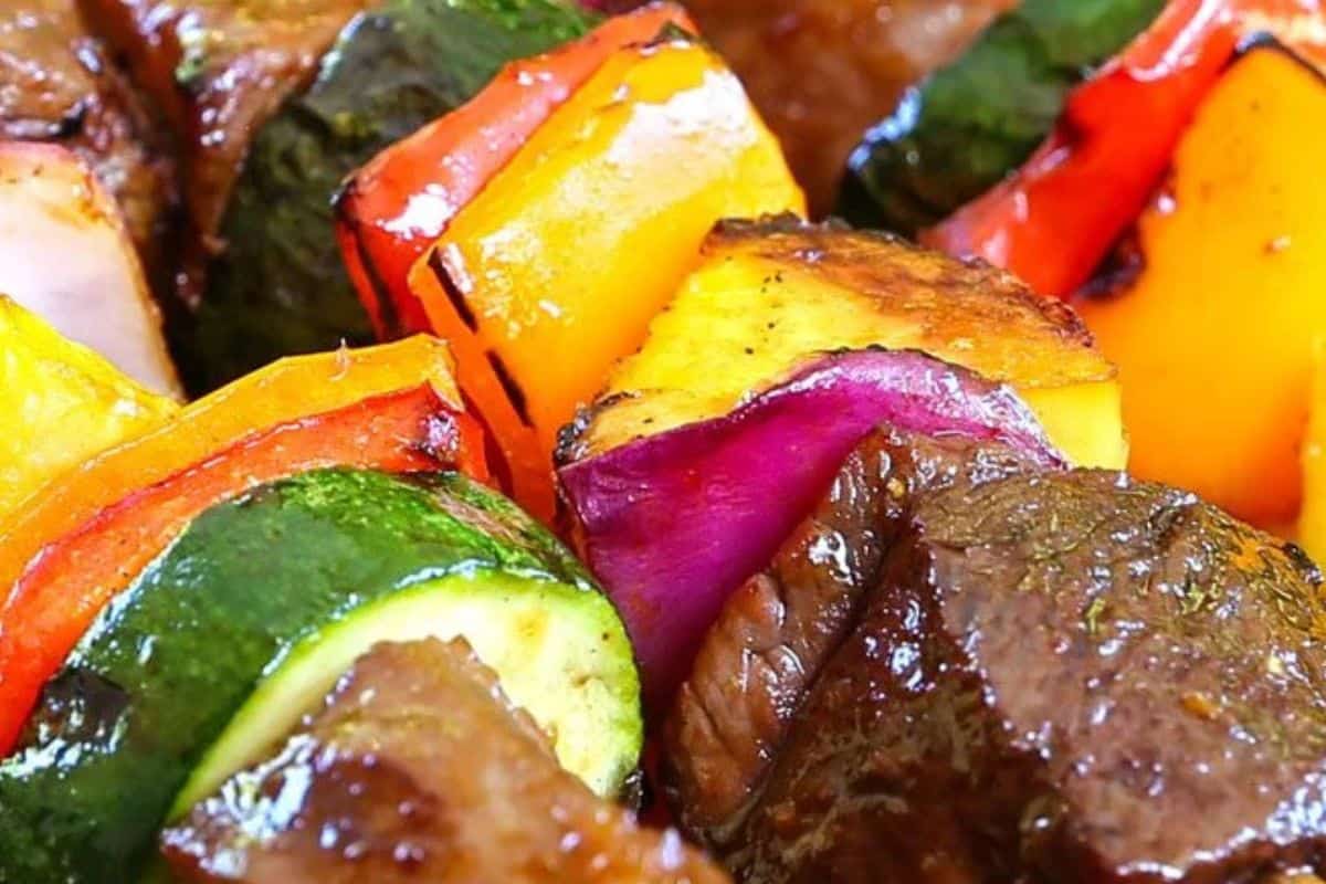 Close-up of grilled beef and vegetable kabobs, featuring pieces of zucchini, red onion, yellow bell pepper, pineapple, and red bell pepper—perfect for your favorite kabob recipes.