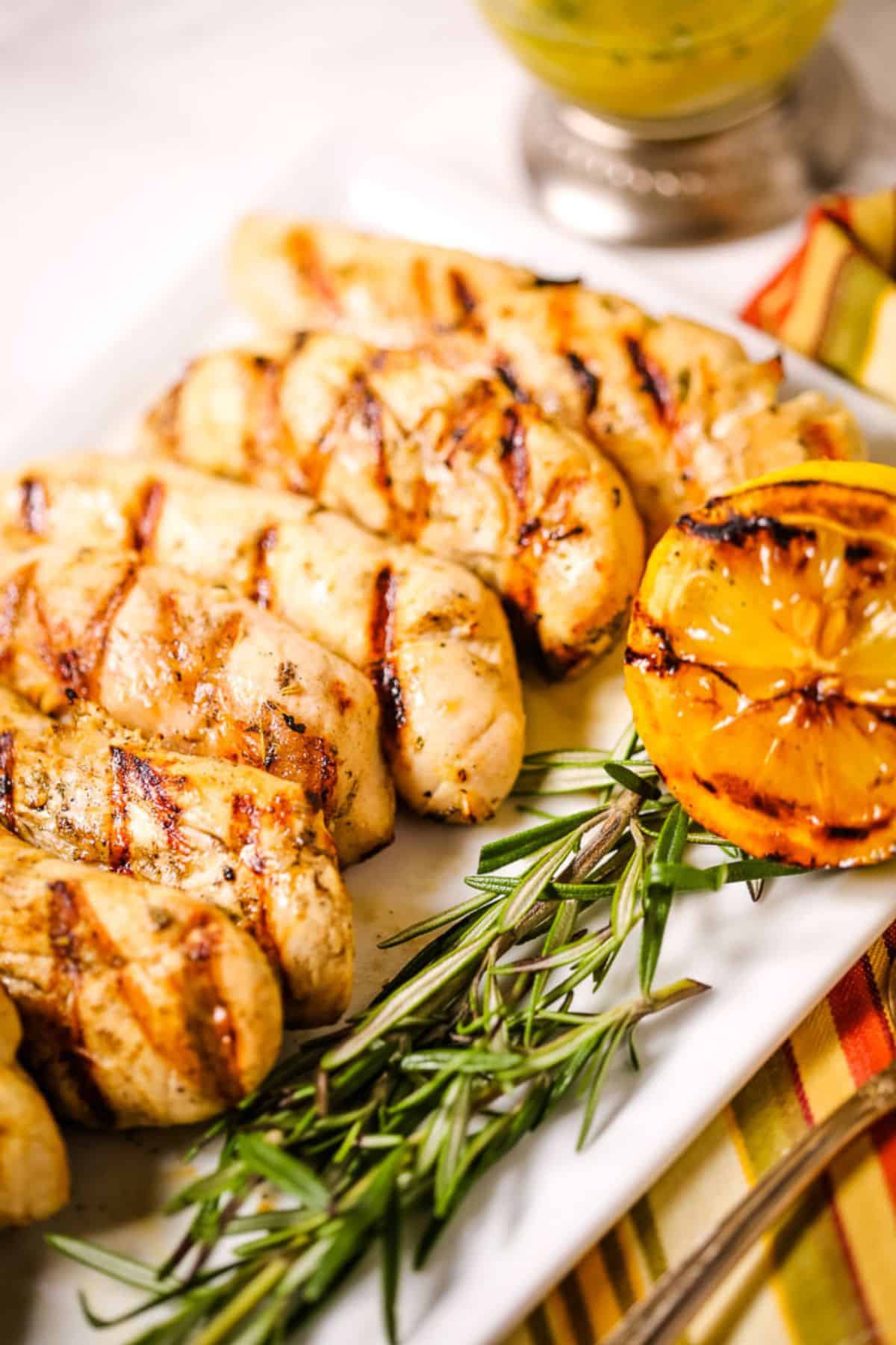Slices with char marks on a white plate and garnished with rosemary sprigs and half a grilled lemon.