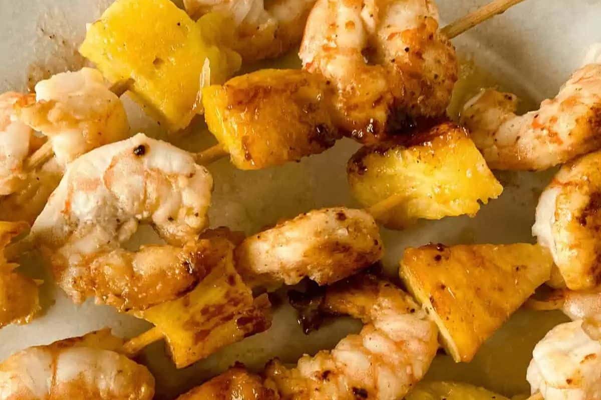 Grilled shrimp and pineapple chunks are skewered on wooden sticks to create a vibrant kabob, shown on a white plate—perfect for adding to your collection of kabob recipes.