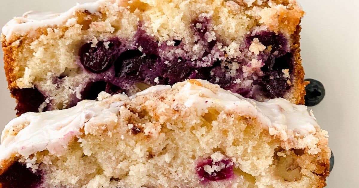 A close-up of two slices of Lemon Blueberry Loaf with a light glaze on top, showing the crumb texture and visible blueberries inside.