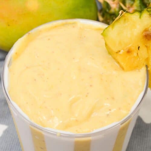 A mango pineapple smoothie with fruit on the side.