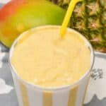 A yellow striped cup with mango pineapple smoothies.