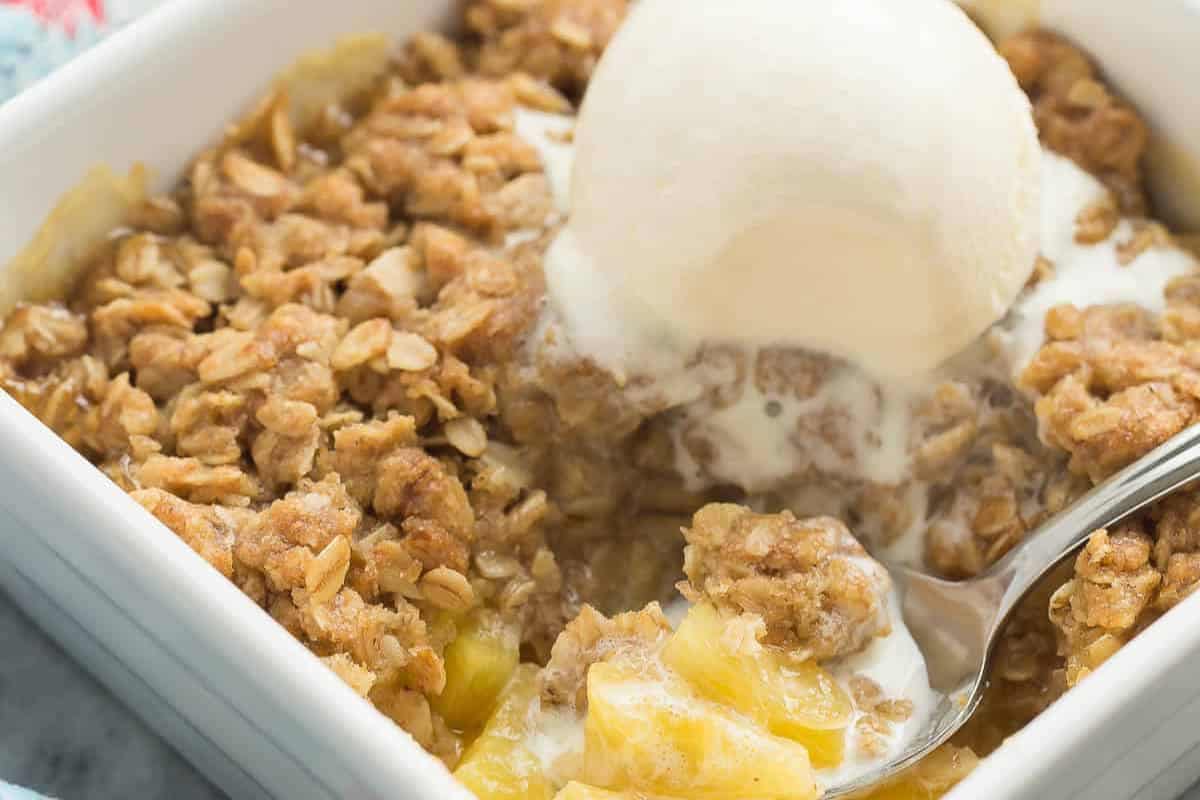 A close-up of a mouthwatering fruit crisp, topped with a scoop of melting vanilla ice cream and a spoon taking a bite—this is one of those pineapple recipes you must try.