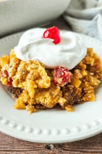 A white dish of the pineapple dump cake with a cherry on top.