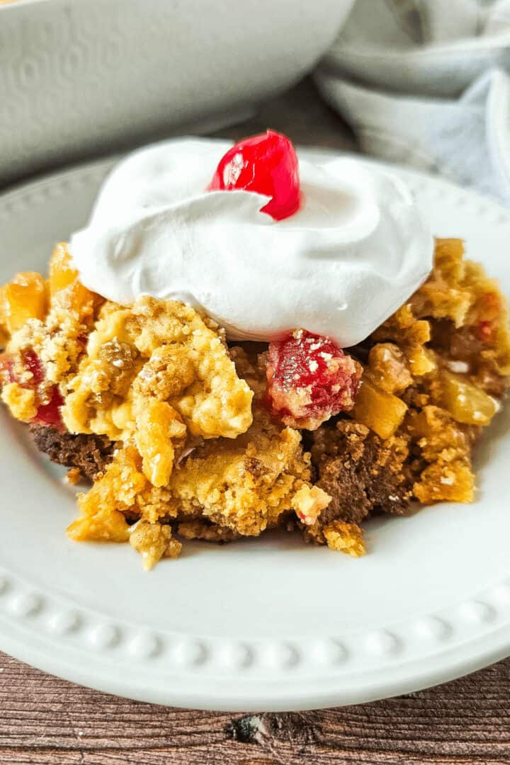 A white dish of the pineapple dump cake with a cherry on top.
