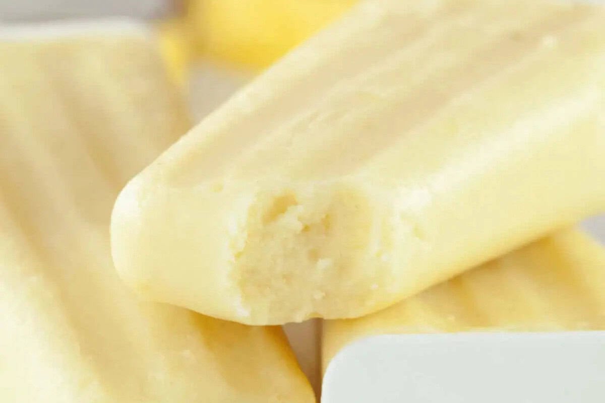 Close-up of three creamy yellow popsicles stacked, with one showing a bite taken out of it—these are a must try for fans of mouthwatering pineapple recipes.