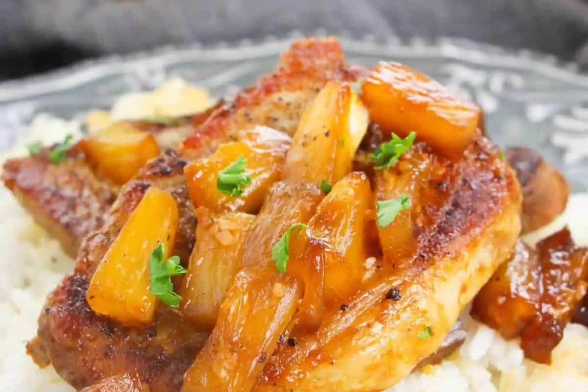 A must-try pork chop topped with pineapple chunks and sauce, garnished with chopped parsley, served on a bed of white rice—perfect for fans of mouthwatering Pineapple recipes.