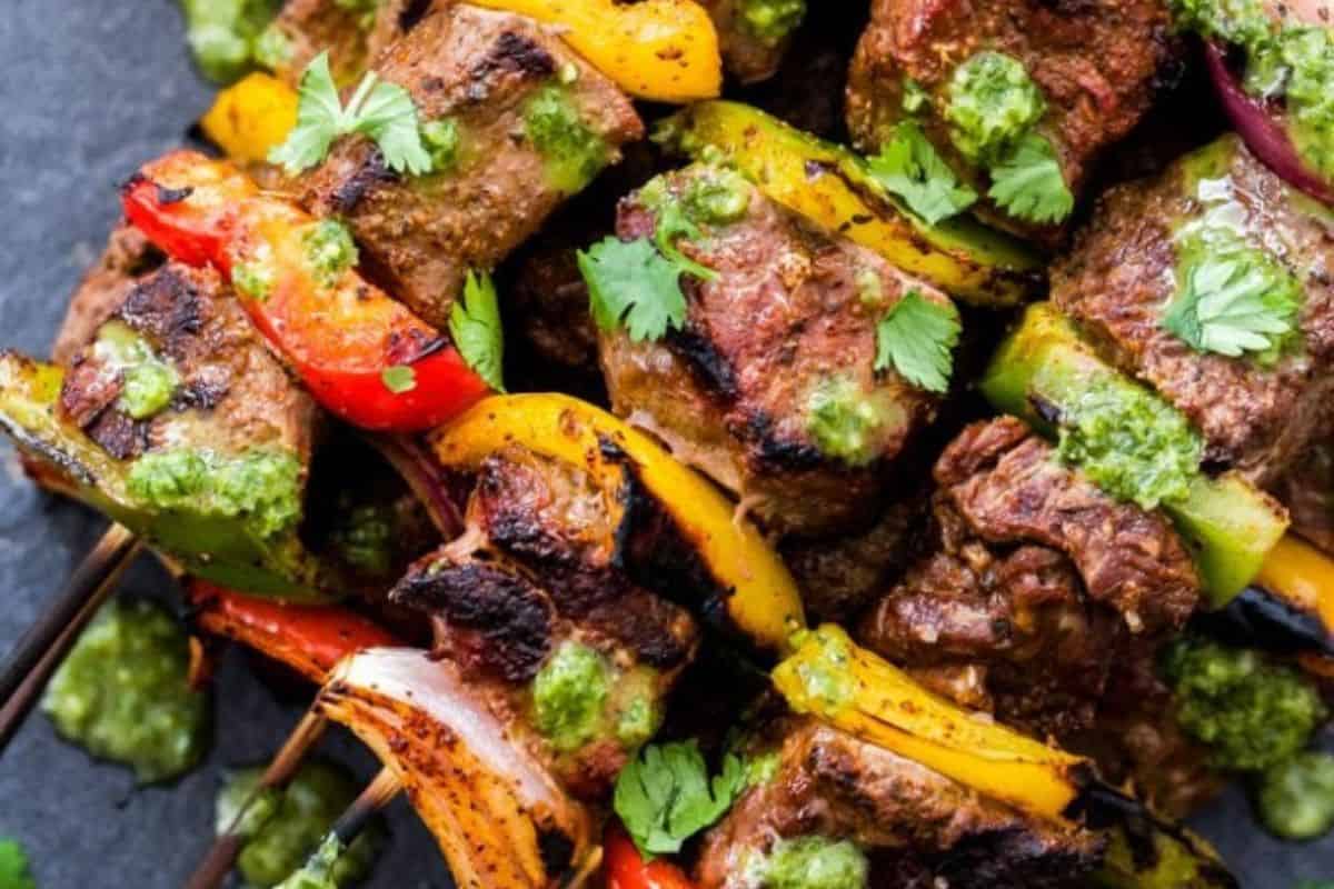 Grilled beef and vegetable kabobs on skewers, garnished with green herb sauce and fresh cilantro—a must-try for anyone who loves kabob recipes.
