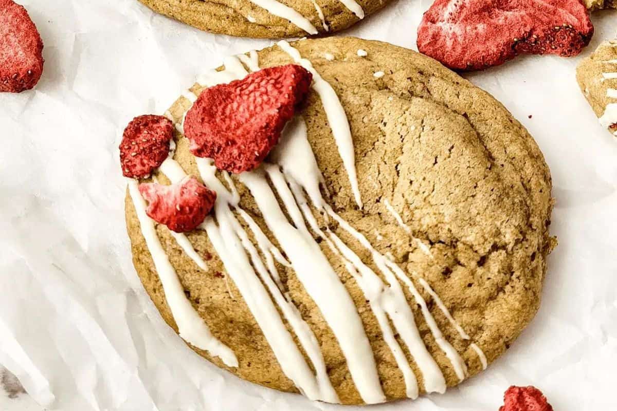Close-up of a strawberry cheesecake cookie, garnished with a drizzle and dried strawberry pieces.