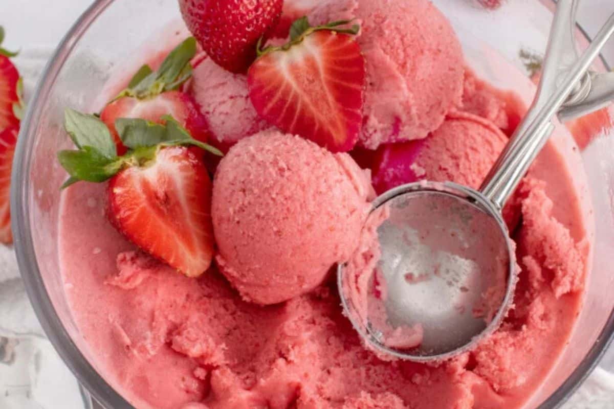 Close-up of a glass bowl of strawberry gelato, topped with strawberries.
